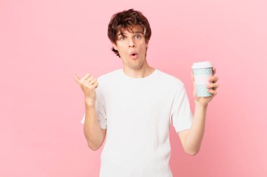 Kahvesi olan genç adam, inançsızlıktan şaşkın şaşkın bakıyor.
