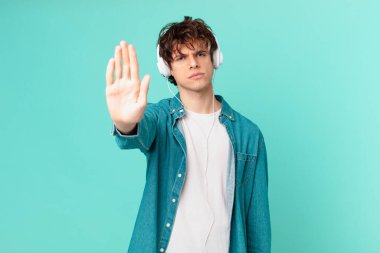 Kulaklıklı genç adam ciddi görünüyor. Avuç içini gösteriyor. Durdurma hareketi yapıyor.