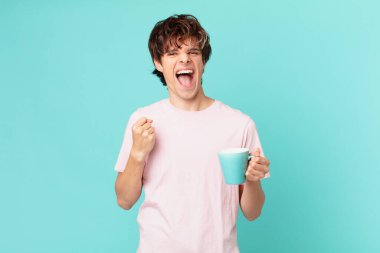 Elinde kahve fincanı olan genç adam şokta, gülüyor ve başarıyı kutluyor.