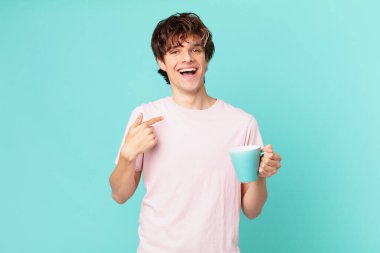 Elinde kahve fincanı olan genç adam mutlu ve heyecanlı bir şekilde kendini işaret ediyor.