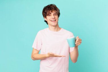 Elinde kahve fincanı olan genç adam neşeyle gülümsüyor, mutlu hissediyor ve bir konsept gösteriyor.