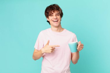 Elinde kahve fincanı olan genç bir adam neşeyle gülümsüyor, mutlu hissediyor ve bir tarafı işaret ediyor.
