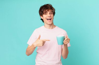 Elinde kahve fincanı olan genç adam heyecanlı ve şaşırmış görünüyor.