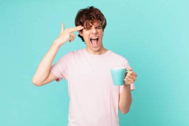 Elinde kahve fincanı olan genç adam mutsuz ve stresli görünüyor, intihar jesti silah işareti yapıyor.