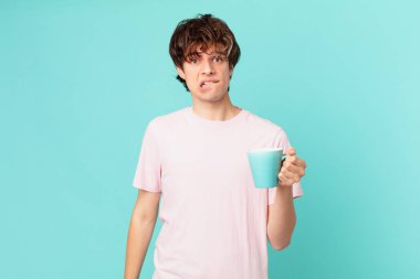 Elinde kahve fincanı olan kafası karışmış ve kafası karışmış genç bir adam.