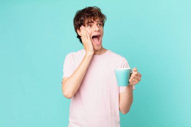 Elinde kahve fincanı olan genç adam mutlu, heyecanlı ve şaşırmış hissediyor.