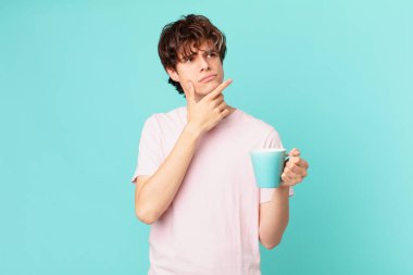 Elinde kahve fincanı olan genç adam, düşünüyor, kuşkulu ve şaşkın hissediyor.