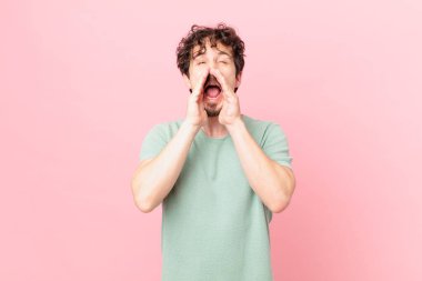 Genç yakışıklı adam mutlu hissediyor, elleri ağızda bağırıyor.