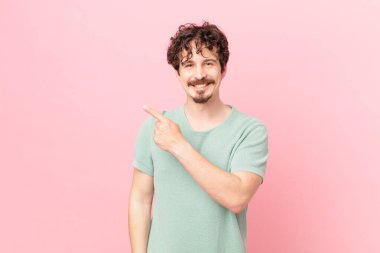 Genç yakışıklı adam neşeyle gülümsüyor, mutlu hissediyor ve bir tarafı işaret ediyor.