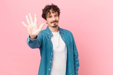 Genç yakışıklı adam gülümsüyor ve arkadaş canlısı görünüyor, beş numarayı gösteriyor.