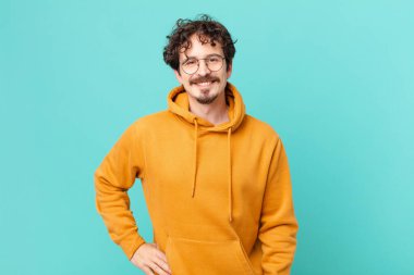 Genç yakışıklı adam mutlu bir şekilde gülümsüyor, eli kalçasında ve kendinden emin.