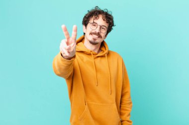 Genç yakışıklı adam gülümsüyor ve mutlu görünüyor, zafer ya da barış işareti yapıyor.