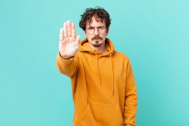 Genç ve yakışıklı adam ciddi görünüyor. Avuç içi gösteriyor. Durdurma hareketi yapıyor.