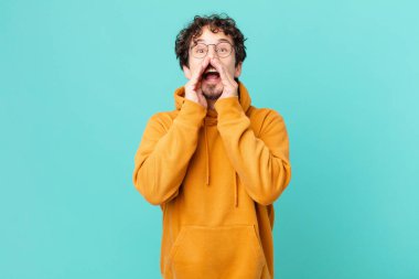 Genç yakışıklı adam mutlu hissediyor, elleri ağızda bağırıyor.