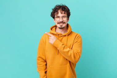 Genç yakışıklı adam neşeyle gülümsüyor, mutlu hissediyor ve bir tarafı işaret ediyor.