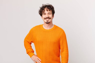 Genç yakışıklı adam mutlu bir şekilde gülümsüyor, eli kalçasında ve kendinden emin.