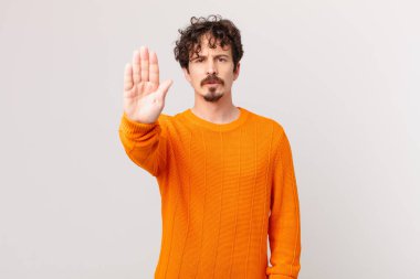Genç ve yakışıklı adam ciddi görünüyor. Avuç içi gösteriyor. Durdurma hareketi yapıyor.