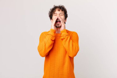 Genç yakışıklı adam mutlu hissediyor, elleri ağızda bağırıyor.