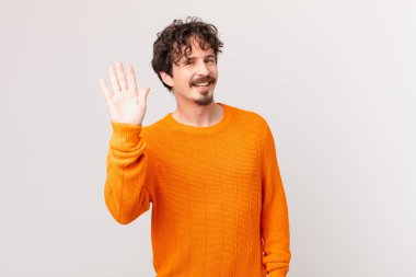 Genç yakışıklı adam mutlu bir şekilde gülümsüyor, el sallıyor, seni selamlıyor ve selamlıyor.