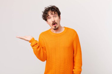 Genç yakışıklı adam şaşırmış ve şok olmuş görünüyor, çenesi düşmüş bir nesne tutuyor.