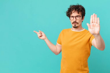 Genç ve yakışıklı adam ciddi görünüyor. Avuç içi gösteriyor. Durdurma hareketi yapıyor.