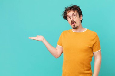 Genç yakışıklı adam şaşırmış ve şok olmuş görünüyor, çenesi düşmüş bir nesne tutuyor.