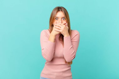 Genç ve güzel bir kadın şok olmuş bir şekilde elleriyle ağzını kapatıyor.