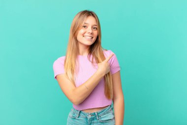 Genç, güzel bir kadın neşeyle gülümsüyor, mutlu hissediyor ve bir tarafı işaret ediyor.