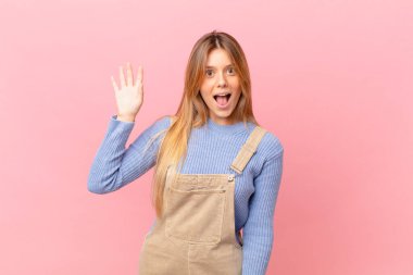 Genç bayan mutlu bir şekilde gülümsüyor, el sallıyor, sizi selamlıyor ve selamlıyor.