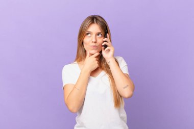 Cep telefonu ile düşünen, kuşkulu ve kafası karışık genç bir kadın.