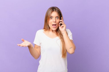 Cep telefonlu genç bir kadın şok olmuş ve şaşırmış hissediyor.