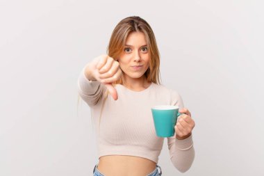 Elinde kahve fincanı olan genç bir kadın kızgın, baş parmağını kaldırıyor.