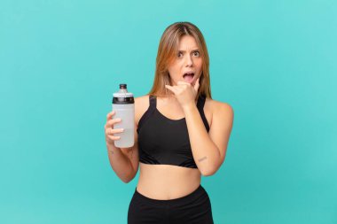 Ağzı ve gözleri açık, elleri çenesinde genç ve güzel bir fitness kadını.