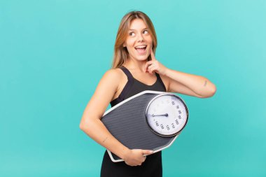 Genç ve güzel spor kadını mutlu bir şekilde gülümsüyor ve hayal kuruyor ya da şüphe ediyor.