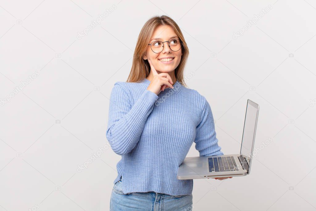 young woman with a laptop smiling happily and daydreaming or doubting