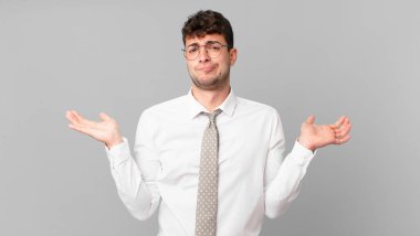 Genç işadamı şaşkın ve şaşkın hissediyor, şüpheci, farklı seçenekleri tartıyor ya da komik ifadeyle seçiyor.