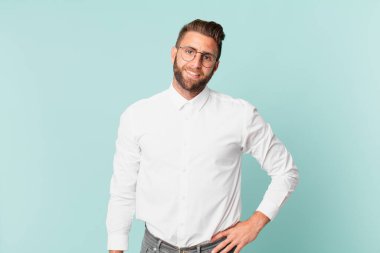 Genç yakışıklı adam mutlu bir şekilde gülümsüyor, eli kalçasında ve kendinden emin.