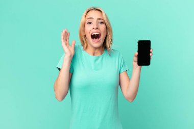 Genç sarışın kadın kendini mutlu ve şaşkın hissediyor. İnanılmaz bir şey ve elinde akıllı bir telefon var.
