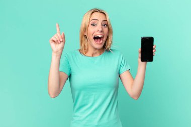 Genç sarışın kadın, bir fikri fark ettikten ve elinde akıllı bir telefon tutduktan sonra mutlu ve heyecanlı bir dahi gibi hissediyor.