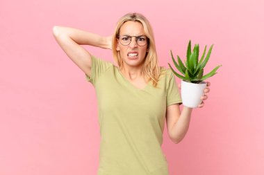 Genç sarışın kadın kendini stresli, endişeli ya da korkmuş hissediyor, elleri başının üstünde ve elinde bir kaktüs tutuyor.