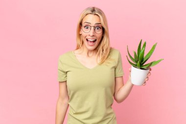 Genç sarışın kadın şok olmuş ya da şaşırmış görünüyor ve elinde bir kaktüs tutuyor.