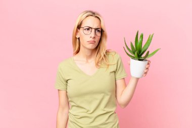 Genç sarışın kadın üzgün, üzgün ya da kızgın hissediyor ve bir tarafa bakıyor ve kaktüs tutuyor.