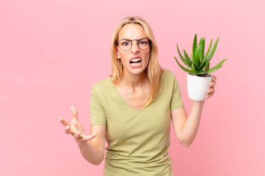 Genç sarışın kadın kızgın, sinirli ve hayal kırıklığına uğramış ve elinde bir kaktüs tutuyor.