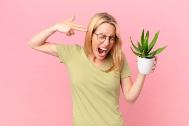 Genç sarışın kadın mutsuz ve stresli görünüyor, intihar işareti yapıyor ve elinde bir kaktüs tutuyor.