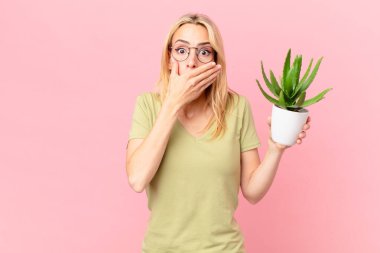 Sarışın genç bir kadın elleriyle ağzını kapatıyor ve elinde bir kaktüs tutuyor.