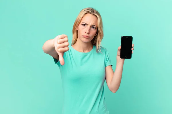 Młoda Blondynka Uczucie Krzyżyk Pokazując Kciuki Dół Trzymając Smartfon — Zdjęcie stockowe