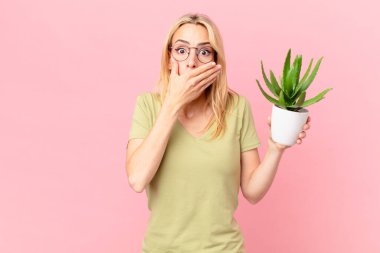 Sarışın genç bir kadın elleriyle ağzını kapatıyor ve elinde bir kaktüs tutuyor.