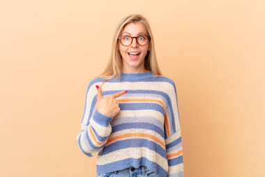 Genç sarışın kadın şok olmuş ve şaşırmış görünüyor, ağzı açık, kendini işaret ediyor.