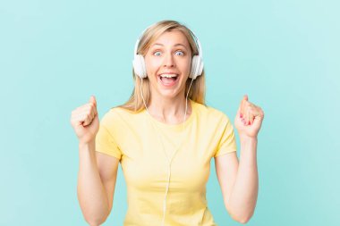 young blonde woman feeling shocked,laughing and celebrating success and listening music.