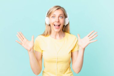 young blonde woman feeling happy and astonished at something unbelievable and listening music.